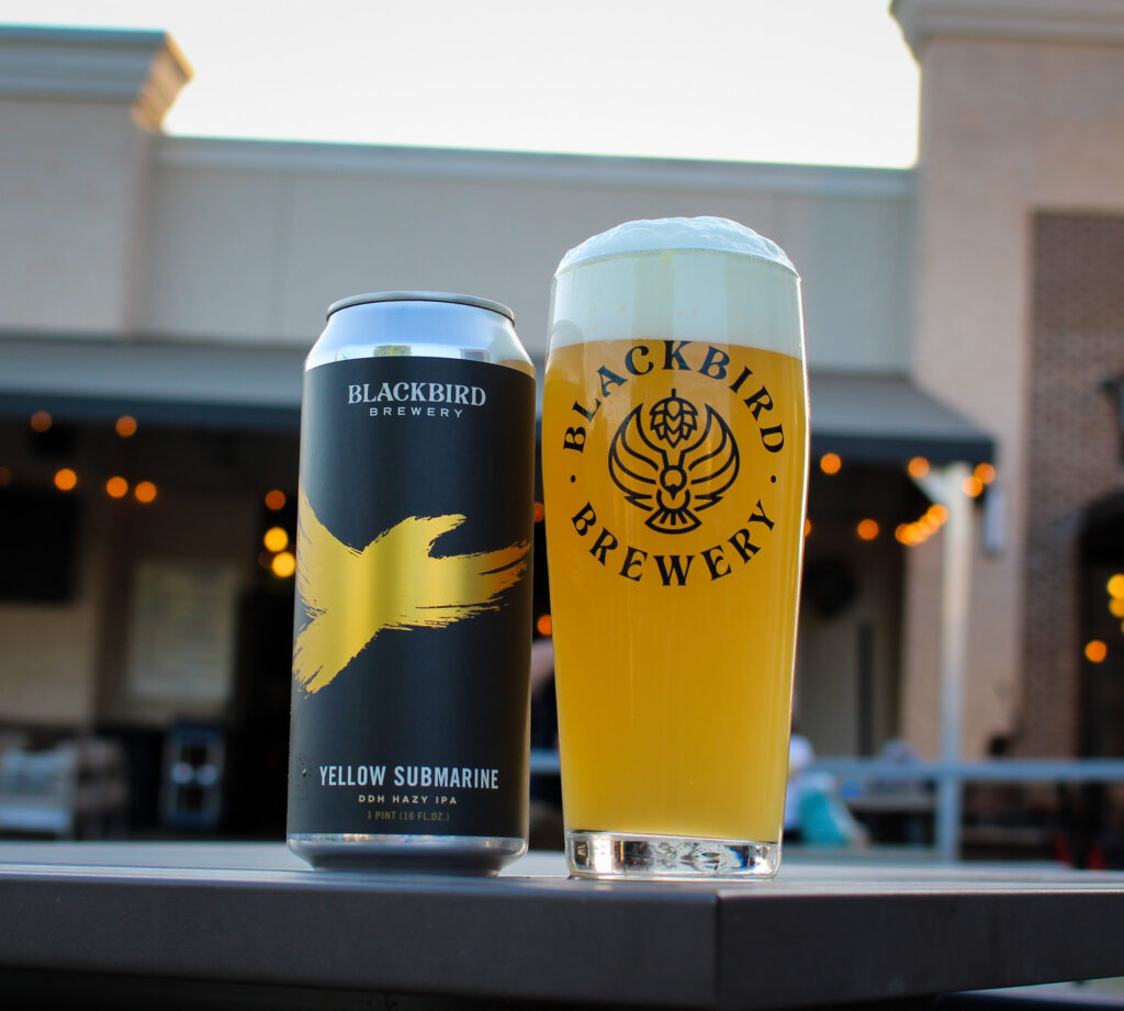 Two beer containers on a table: Blackbird Yellow Submarine can beside a pint of Blackbird Brewery beer in a glass.